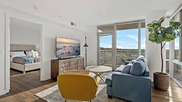 A modern living room with a sofa, a yellow chair, a TV, and a large window with a view.