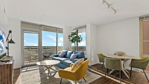 A modern living room with a blue sofa, yellow armchair, and a dining table with chairs.