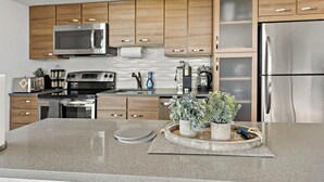 A modern kitchen with wooden cabinets, stainless steel appliances, and a granite countertop. - Tysons 2BR | Panoramic Views, Rooftop Pool & Gym (McLean)