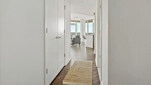 A hallway with white walls and wooden flooring, leading to a living area with a sofa and a coffee table. - Tysons 2BR | Panoramic Views, Rooftop Pool & Gym (McLean)
