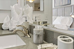 A modern bathroom with a large mirror, a gold faucet, and white towels.