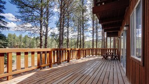 A wooden deck with a railing, a picnic table, and a view of a forest.