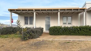 Ett modernt hus med en inglasad veranda, en ytterdörr och en liten trädgårdsdel med buskar och en grusgång.