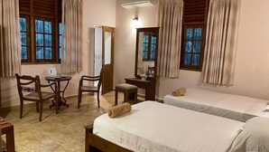 Une chambre d’hôtel avec deux lits, un bureau avec une chaise, une petite table et une fenêtre avec des rideaux.
