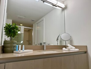 Een moderne badkamer met een grote spiegel, een wastafel, een plant en toiletartikelen.