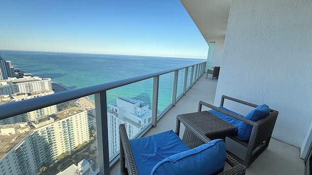 A balcony with wicker furniture, a view of the ocean, and high-rise buildings in the background.