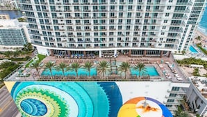 A high-rise hotel with a rooftop pool area, multiple balconies, and a large mural.