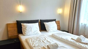 Un lit double avec du linge de lit blanc et deux oreillers, une tête de lit en bois et deux tables de chevet.