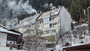 Un bâtiment moderne doté de panneaux solaires sur le toit, entouré d’arbres couverts de neige et avec une chaîne de montagnes en arrière-plan.