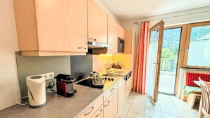 Une cuisine avec des meubles en bois, un four à micro-ondes, une bouilloire et une cuisinière. Il y a une fenêtre avec des rideaux et une vue sur la verdure à l’extérieur.