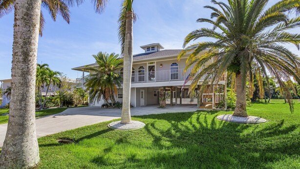 A large, two-story house with a balcony, surrounded by palm trees and a well-maintained lawn. - Bokeelia Bliss! 3/3 Heated Pool, Boat Ramp Included! (Bokeelia)