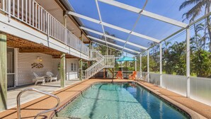 An indoor swimming pool with a glass ceiling, a staircase leading to a balcony, and outdoor seating. - Bokeelia Bliss! 3/3 Heated Pool, Boat Ramp Included! (Bokeelia)