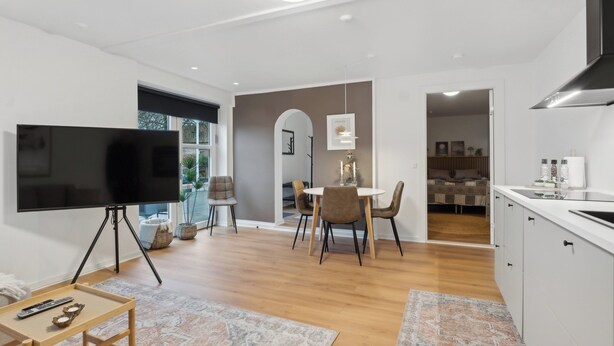 Un salon moderne doté d’un téléviseur à écran plat, d’un coin repas avec une table et des chaises, et d’une cuisine équipée de placards et d’une cuisinière.