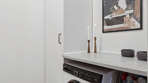 Une buanderie moderne équipée d’un lave-linge, d’un étendoir et d’une œuvre d’art encadrée accrochée au mur.