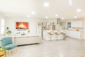 A modern kitchen with white cabinetry, a central island with bar stools, and a fireplace.