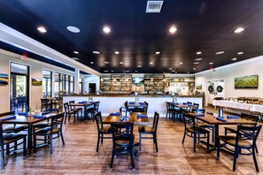 Un ristorante con diversi tavoli e sedie, un'area bar e vista sull'esterno.