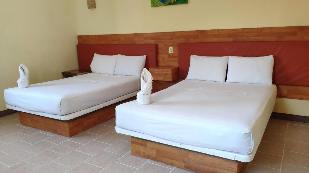 Dos camas individuales con cabeceros de madera y ropa de cama blanca, dispuestas una al lado de la otra en una habitación con suelo de baldosas.