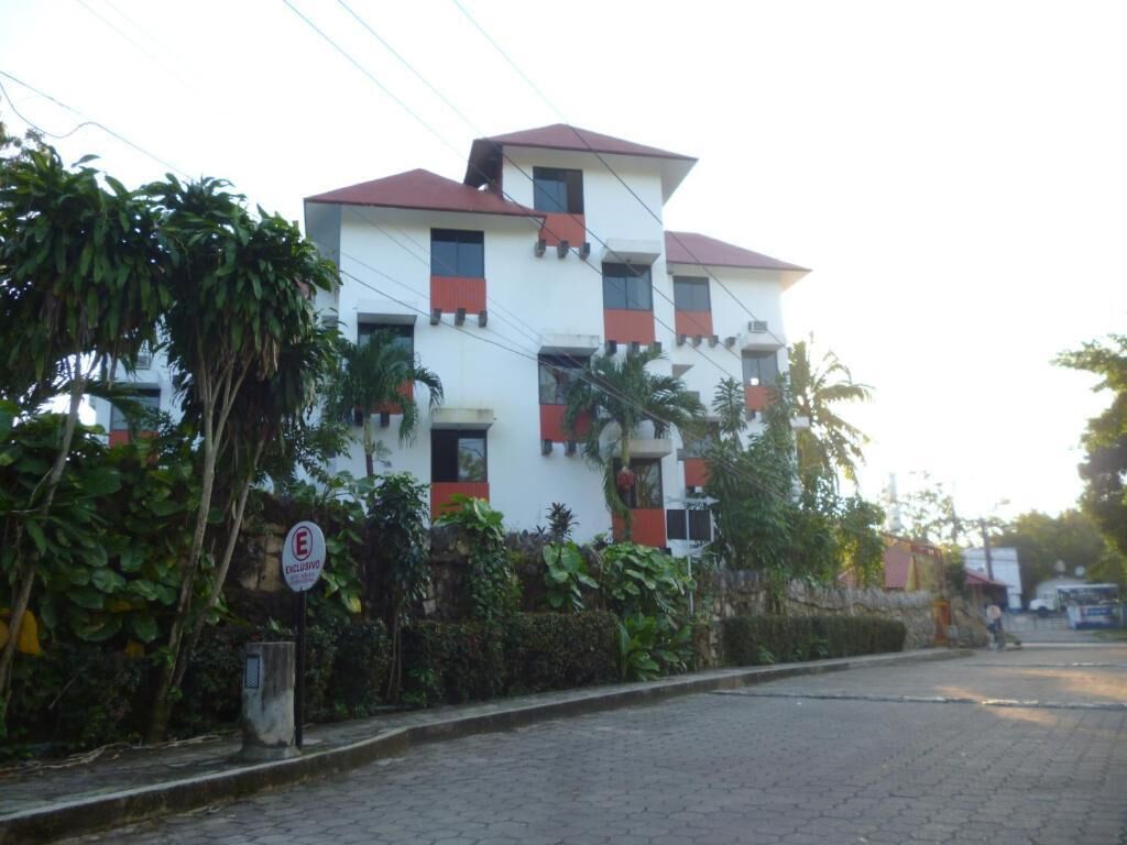 A multi-story building with a red roof and white walls, surrounded by greenery.