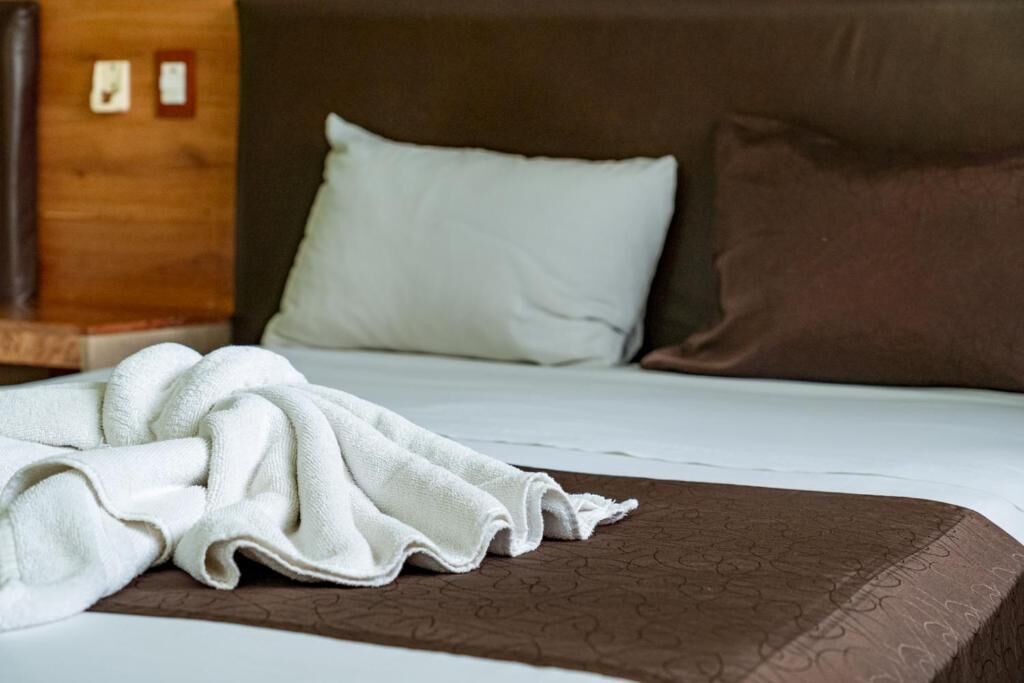 A neatly made bed with a brown bedspread and two pillows, one white and one brown.