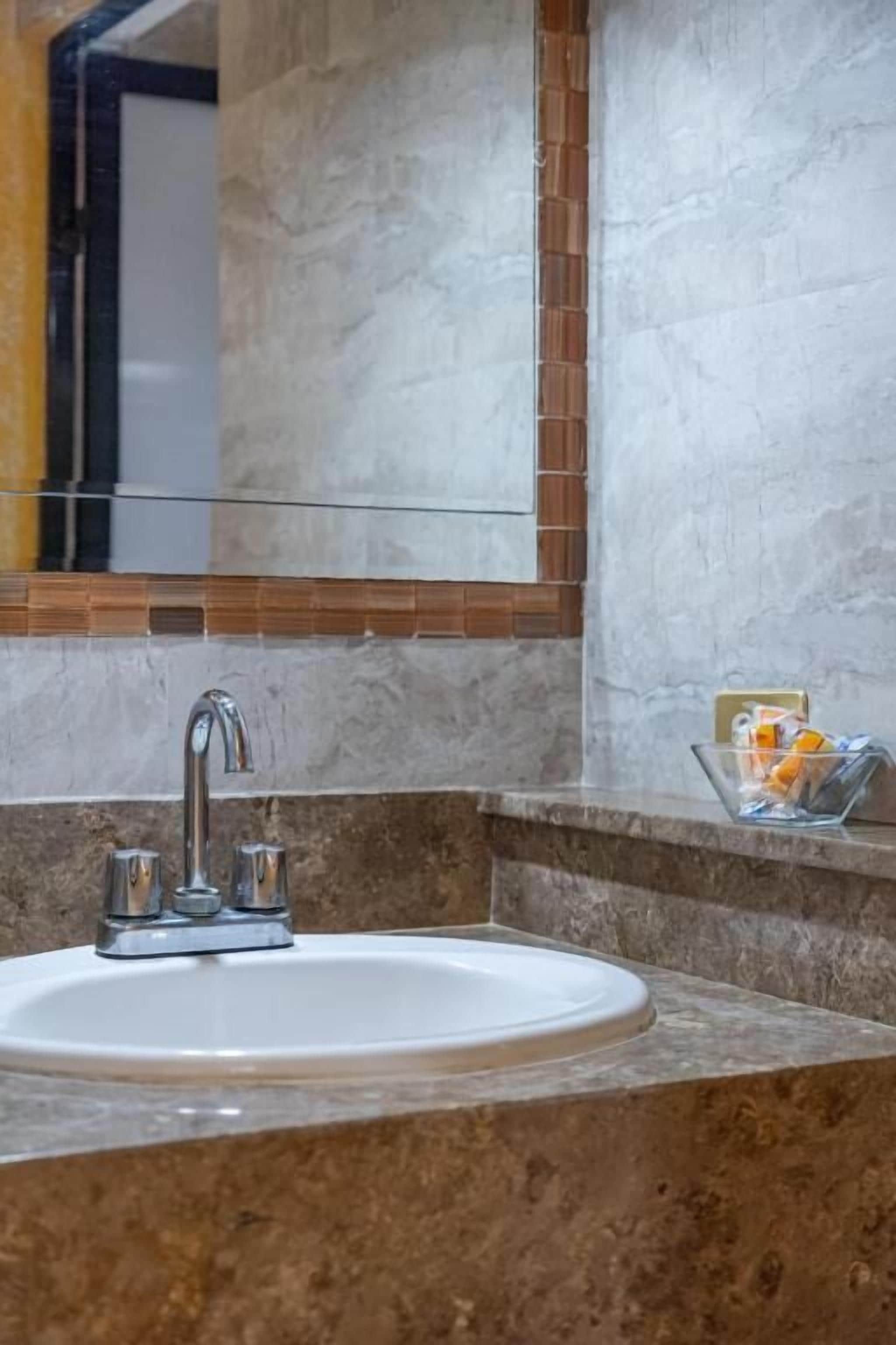 Une salle de bain avec un lavabo blanc, un miroir et un porte-savon en verre posé sur le comptoir.