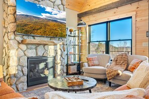 A cozy living room with a stone fireplace, a comfortable sofa, and a large window offering a scenic view.