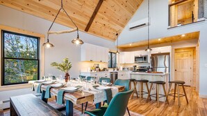 A modern kitchen with wooden cabinets, stainless steel appliances, and a dining area with a wooden table and chairs. - Luxury Mountain Lodge | Hot Tub, Mtn Views, Sauna,  Game Room, Fire Pit (Bethel)