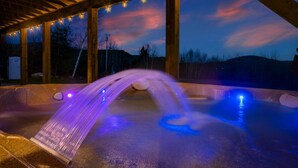 A hot tub with a waterfall feature, surrounded by wooden beams and string lights. - Luxury Mountain Lodge | Hot Tub, Mtn Views, Sauna,  Game Room, Fire Pit (Bethel)