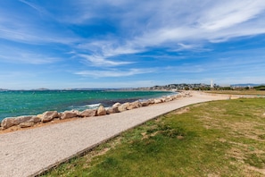 A coastal walkway with a stone barrier, grassy areas, and a distant view of a cityscape including a tower. - Apartment 'L'Esperance' with Mountain View, Wi-Fi and Air Conditioning (Marseille)