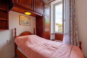 A bedroom with a wooden bed, a window with curtains, a painting on the wall, and built-in wooden cabinets.
