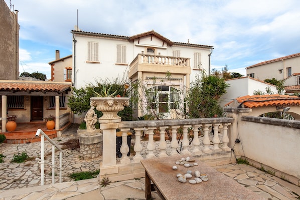 A traditional Mediterranean-style building with a stone staircase, a balcony with a balustrade, and a stone table with a few items on it.