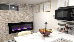 Una cocina moderna con pared de piedra, televisor de pantalla plana, microondas y frutero en la encimera.