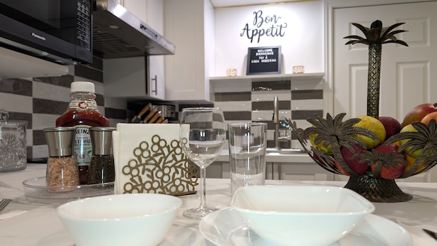 Una encimera de cocina con dos tazones blancos, un vaso de agua, condimentos y un frutero decorativo.