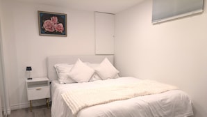 Un dormitorio con cama, mesita de noche blanca y un cuadro de rosas.