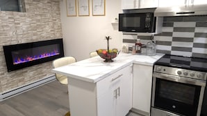 Una cocina moderna con microondas, estufa y horno integrados. Se aprecia una pared de piedra con chimenea, una encimera blanca y un frutero.