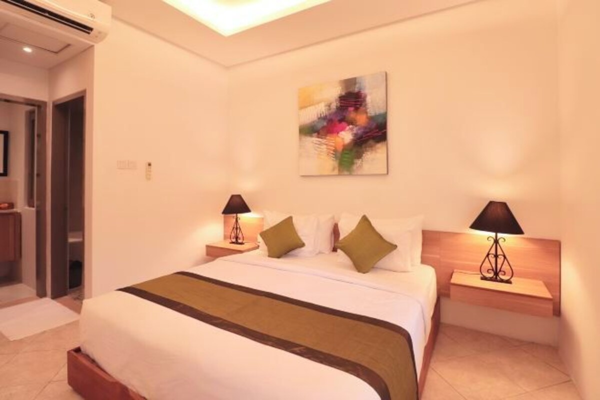 A hotel room with a large bed, two bedside tables with lamps, a painting on the wall, and a door leading to another room.