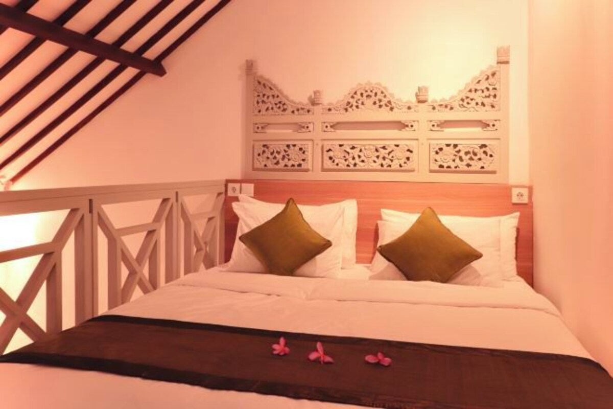 A bed with a wooden headboard, white bedding, and two green pillows.