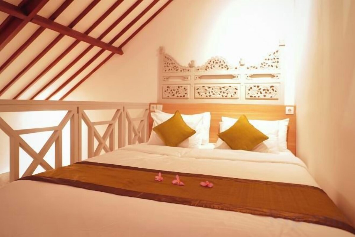 A bedroom with a wooden ceiling, a bed with white bedding and green pillows, and a decorative headboard.