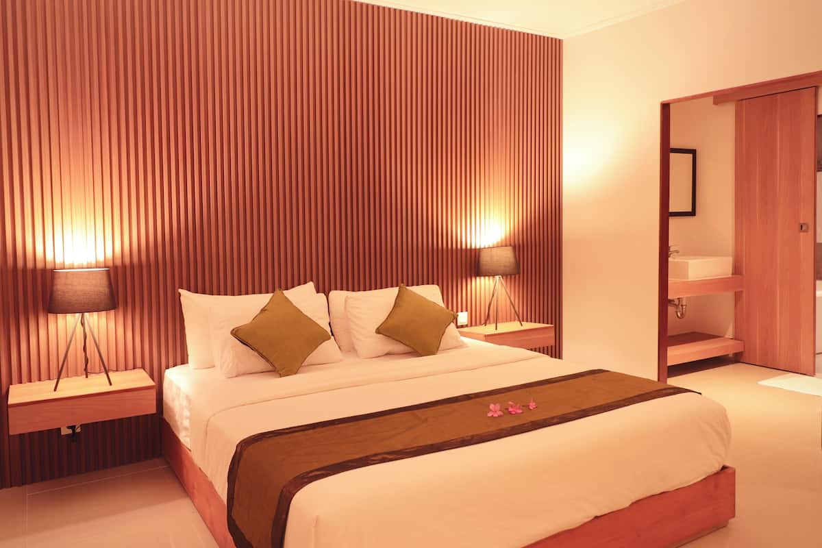 Ein Hotelzimmer mit einem großen Bett, zwei Nachttischen, einem hölzernen Kopfteil, einem Schrank aus Holz und einem Badezimmer mit Waschbecken und Spiegel.