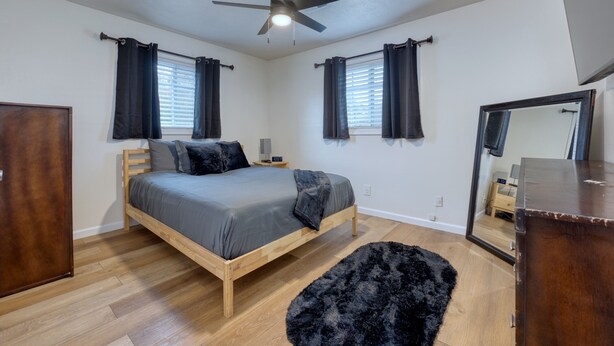 Une chambre à coucher avec un lit en bois, un ventilateur de plafond, un tapis noir et une commode.