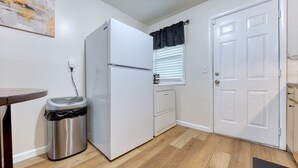 Une cuisine de taille réduite comprenant un réfrigérateur, une poubelle, une fenêtre avec des stores et une porte.