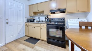 Une cuisine de taille réduite avec des meubles de couleur beige, une cuisinière noire et un réfrigérateur blanc.