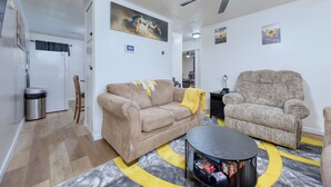 Un salon avec un canapé beige, un plaid jaune, une table basse noire et un ventilateur de plafond.