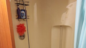 A bathroom with a bathtub, a shower, and a shelf with toiletries. - Morning BNB (Gurugram)