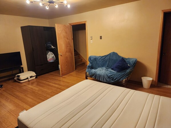 A room with a bed, a TV, a wardrobe, a covered chair, and a staircase. - Morning BNB (Gurugram)