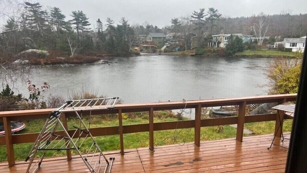 A wooden deck with a metal drying rack, overlooking a lake with houses in the background. - Morning BNB (Gurugram)