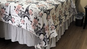 Een slaapkamer met een bed, voorzien van een beddegoed met Parijse thema, een plafondventilator, een lijst met een foto van Parijs en een potplant.