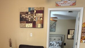 Een woonkamer met een bruine leren bank, een glazen salontafel en een vloerkleed. Er hangt een schilderij aan de muur en een bord boven de deur.