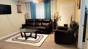 Een woonkamer met een bruine leren bank, een glazen salontafel en een bruine leren fauteuil.