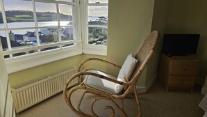 Una habitación con una silla de mimbre junto a una ventana que da a una masa de agua y edificios.