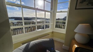 Una habitación con un ventanal grande que da a un lago y colinas, un radiador, una silla y una lámpara.